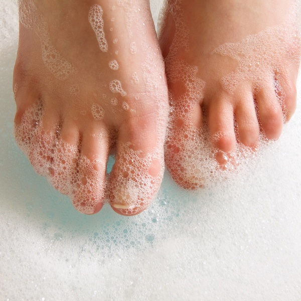 A person cleaning their feet in soapy water - tips for keeping your feet healthy in summer with Chronic Care of Richmond.